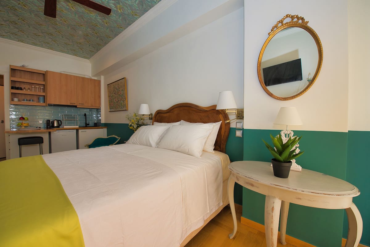 Ein Schlafzimmer mit Bett, Nachttisch und einer kleinen Küchenzeile im Hintergrund.