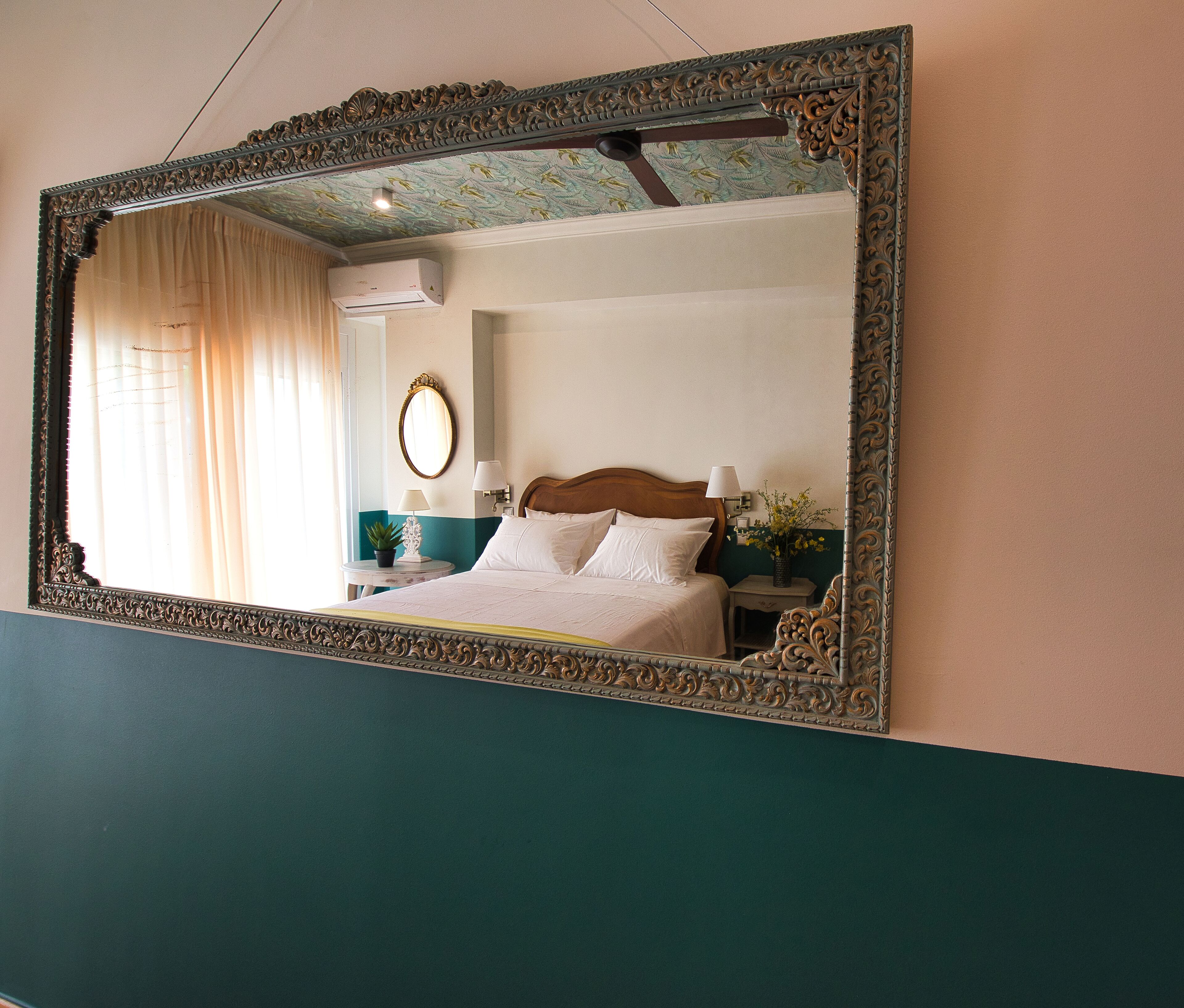 A bedroom with a large ornate mirror, a bed with white linens, a nightstand with a lamp, and a wall-mounted air conditioning unit.