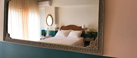 Une chambre dotée d’un grand miroir décoratif, d’un lit avec du linge de lit blanc, d’une table de chevet avec une lampe et d’un climatiseur fixé au mur.