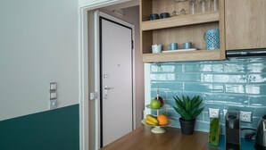 Une cuisine avec une étagère en bois où sont posées des tasses et des verres, un présentoir de fruits et un crédence bleue carrelée.
