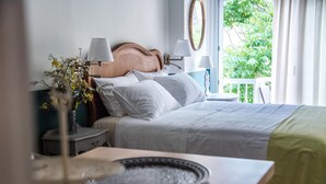 Un lit bien fait, avec du linge de lit blanc, une table de chevet avec une lampe, et une vue sur la verdure à l’extérieur.