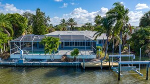 Ein Haus mit einer großen Glaskonstruktion, umgeben von Wasser und Palmen.