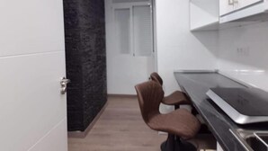 Eine kleine Küche mit weißen Schränken, einer schwarzen Arbeitsplatte und einem braunen Stuhl.