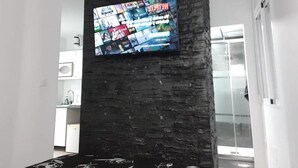 Ein modernes Wohnzimmer mit einem großen Flachbildfernseher an einer strukturierten Wand, einer Couch mit floralem Muster und einer Glastür zu einem weiteren Raum.