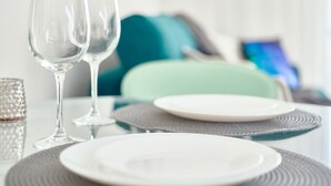 Ruokapöytä on katettu valkoisilla lautasilla, kirkkailla laseilla ja kuvioidulla aluslautasella.