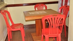 A small dining area with a wooden table and four red plastic chairs. - Square Suites (Mbarara)