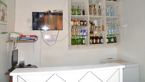 A bar area with shelves of various liquor bottles and glasses, a television mounted on the wall, and a desk with a computer and telephone. - Square Suites (Mbarara)