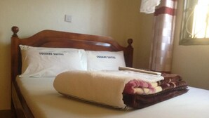 A bed with a wooden headboard, two pillows labeled "SQUARE SUITES," and a folded blanket on the bed. - Square Suites (Mbarara)