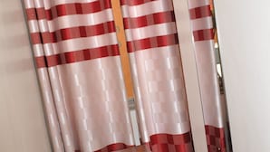 A wooden chair with a magazine, a red and white checkered curtain, and a mirror on the wall. - Square Suites (Mbarara)