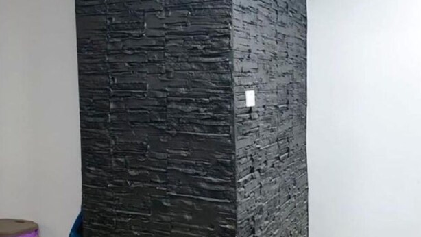 Een kamer met een structuurwand in het zwart, een houten vloer en een witte prullenbak.
