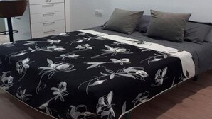 Een slaapkamer met een bed, grijs beddengoed, een zwart-wit bloemenbedekking en een witte garderobe.
