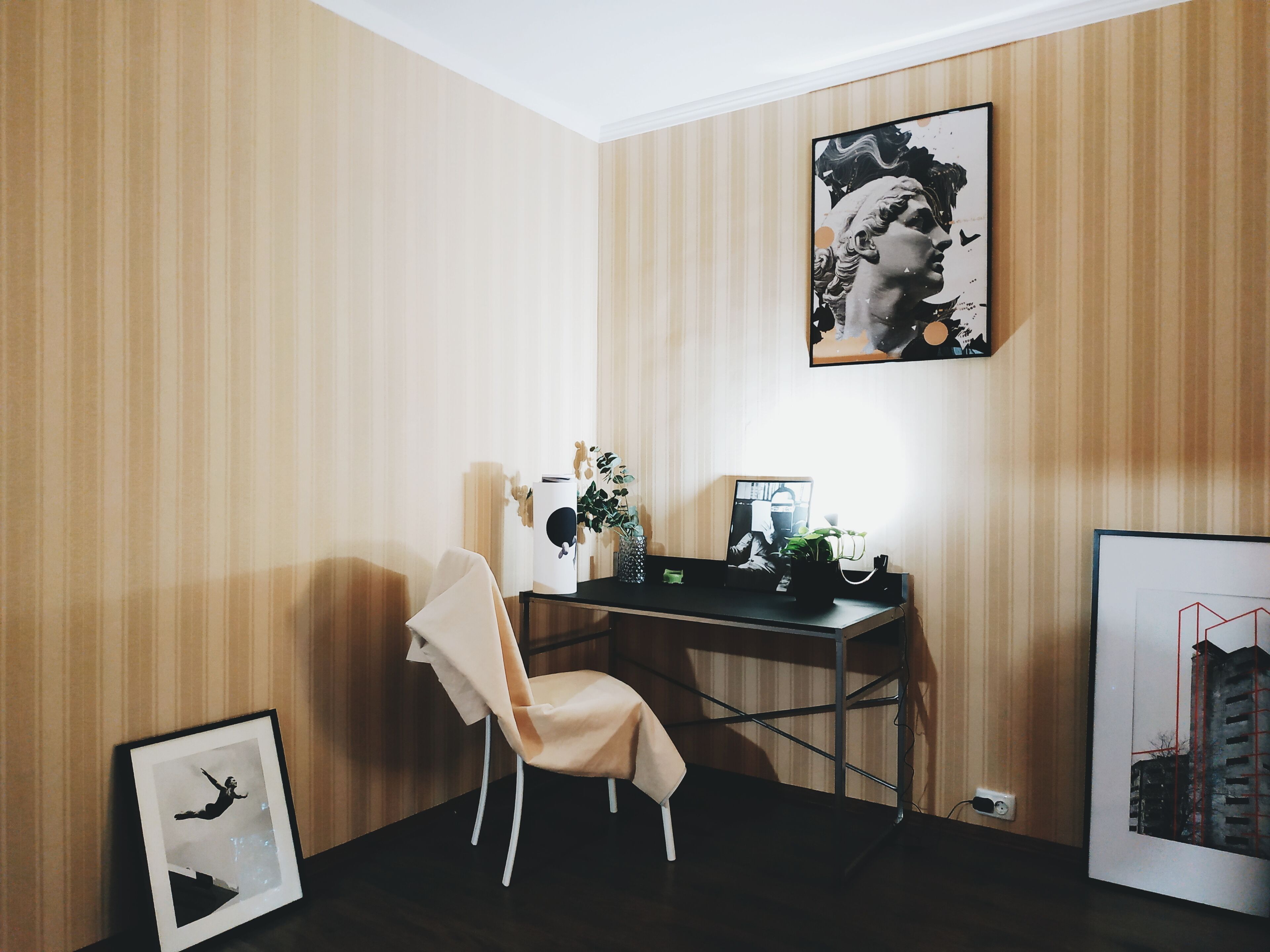 Una habitación con papel tapiz a rayas, un escritorio con una computadora, una silla y obras de arte enmarcadas en las paredes.