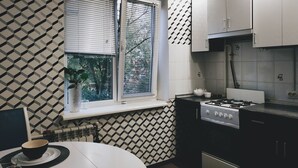 A modern kitchen with a gas stove, white cabinets, and a window with blinds. - MalinaApt Hello Geometry (Kyiv)