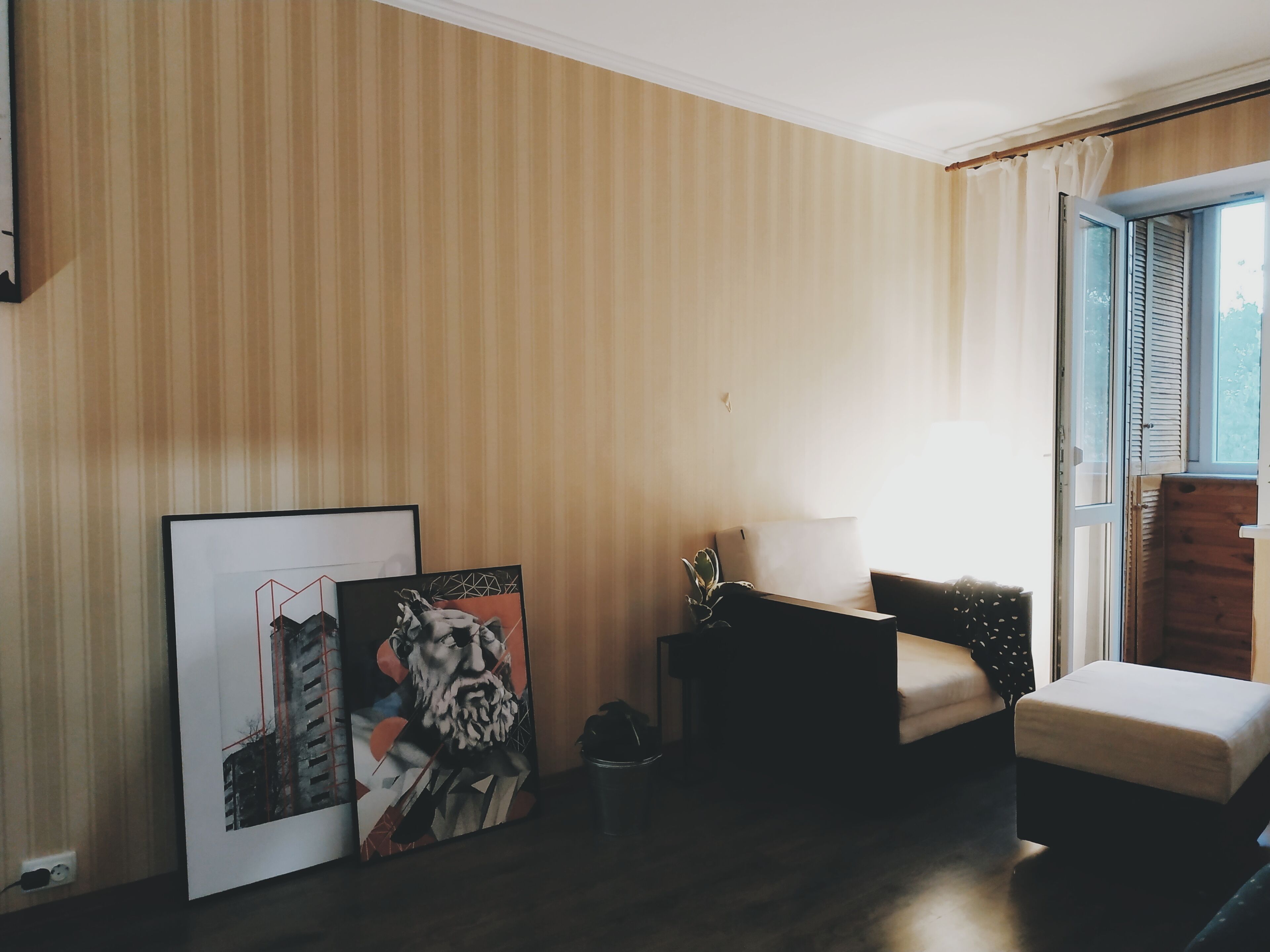 Ein Zimmer mit Streifenmuster-Tapete, einem Sofa, einem kleinen Tisch mit Lampe und einem Fenster mit Fensterläden.