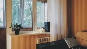 A room with a window, a radiator, a black table, a sofa with patterned cushions, and a potted plant. - MalinaApt Hello Geometry (Kyiv)