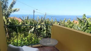 A balcony with two white plastic chairs, a small round table, and a view of the ocean. - Casa da Avó Celina (Funchal)