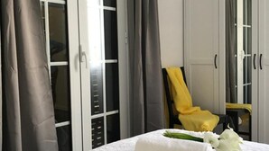 A neatly made bed with a floral bedspread, a stack of white towels, and a chair with a yellow towel. - Casa da Avó Celina (Funchal)
