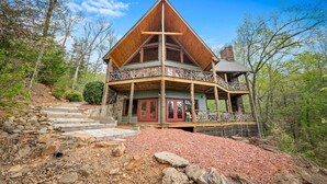 Une cabane dotée d’un toit à forte pente, d’un balcon avec une balustrade et d’un chemin de pierre menant à l’entrée.