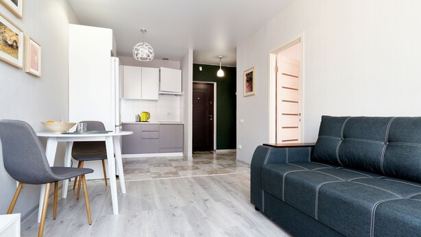 Ein modernes Wohnzimmer mit einer Couch, einem Esstisch mit Stühlen, einer Küchenzeile und einem Flur, der zu einer Tür führt.