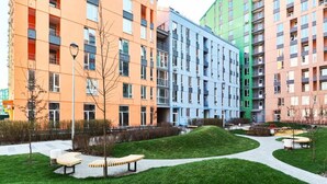Ein moderner Wohnkomplex mit mehreren Gebäuden, einem begrünten Innenhof mit Bänken und einem gepflasterten Weg.