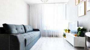 Ein modernes Wohnzimmer mit grauem Sofa, einem weißen Fernsehschrank und einem großen Fenster mit transparenten Vorhängen.