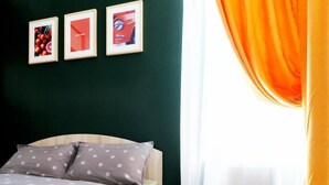 Ein Schlafzimmer mit einem Bett, zwei Kissen, einer Decke und zwei Orangen auf dem Bett. An der Wand hängen drei gerahmte Bilder.