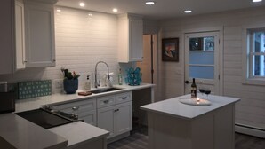 A modern kitchen with white cabinetry, a central island, and recessed ceiling lights. - The Frankfort Surf Cottage (Frankfort)