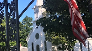 A white church with a steeple and a flagpole with an American flag. - The Frankfort Surf Cottage (Frankfort)