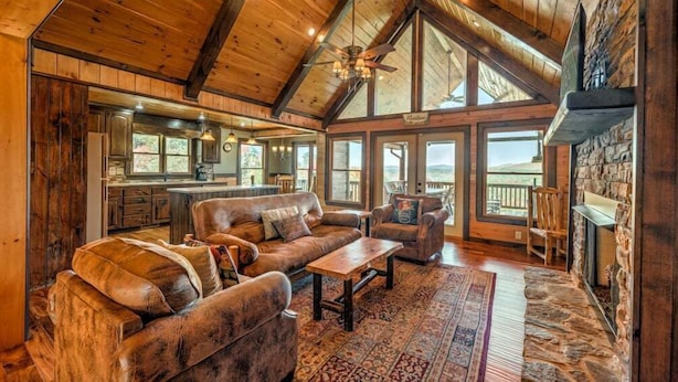 A spacious living room with a high ceiling, wooden beams, a fireplace, and large windows offering a view of the outdoors. - Vista Ridge- Spectacular Views | Relaxing Hot Tub | Master on Main (Blue Ridge)