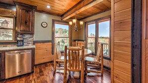 A rustic cabin interior with a wooden dining table, chairs, a chandelier, and a kitchen area with a dishwasher. - Vista Ridge- Spectacular Views | Relaxing Hot Tub | Master on Main (Blue Ridge)