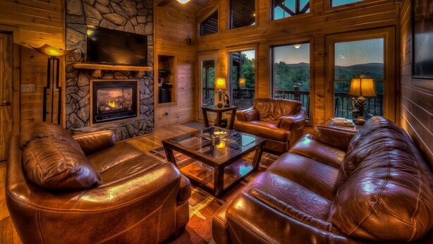 Ein gemütliches Wohnzimmer mit Ledersofas, einem Kamin und großen Fenstern mit Blick ins Freie.