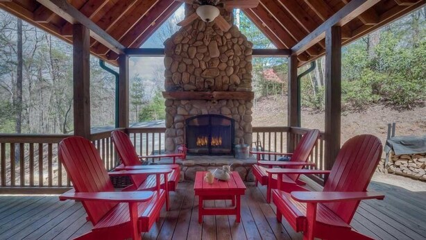 Un espace extérieur aménagé, abrité et doté d’une cheminée en pierre, de fauteuils Adirondack rouges et d’une terrasse en bois.