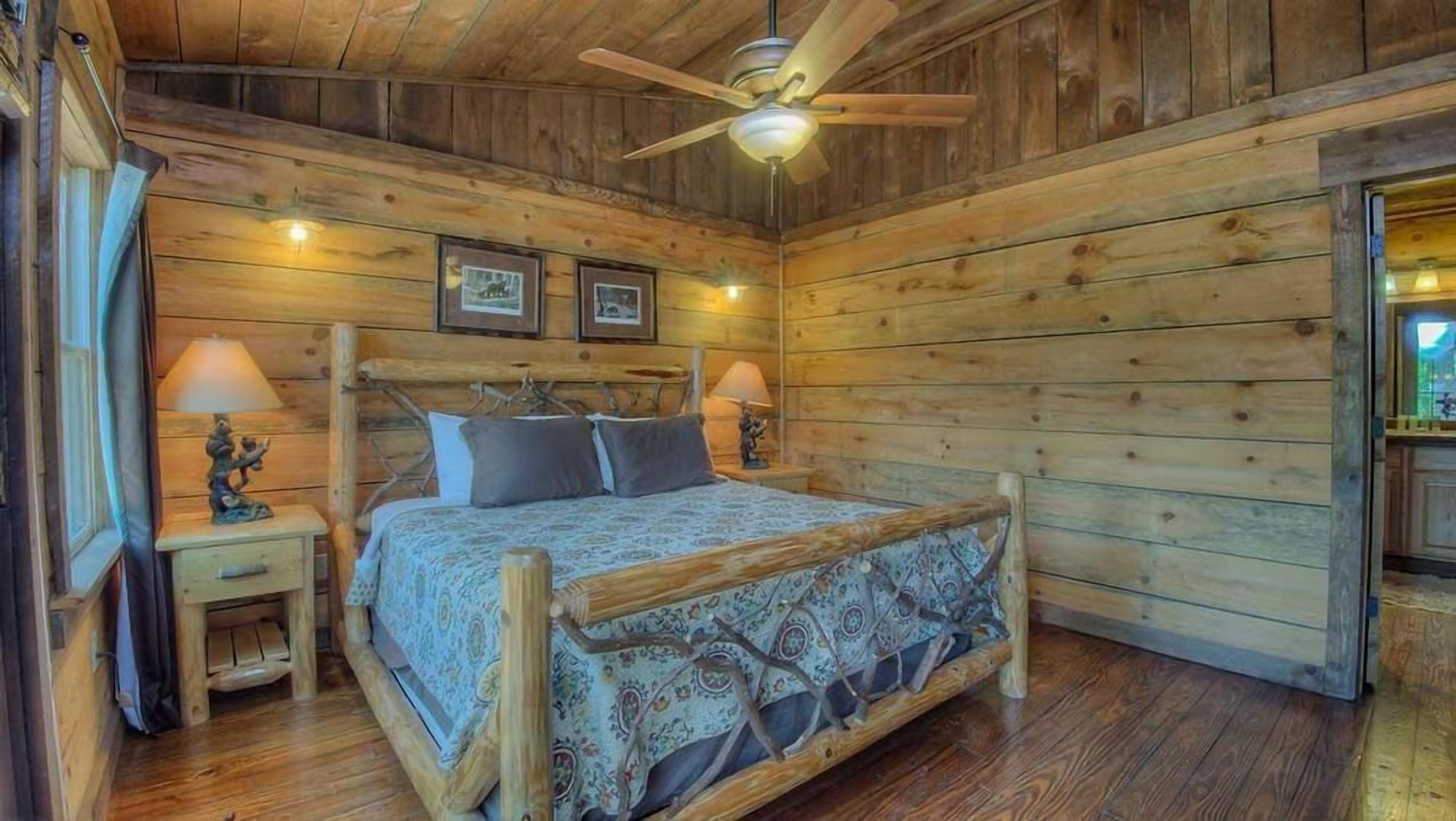 A wooden cabin bedroom with a bed, two nightstands, a ceiling fan, and framed pictures on the wall.