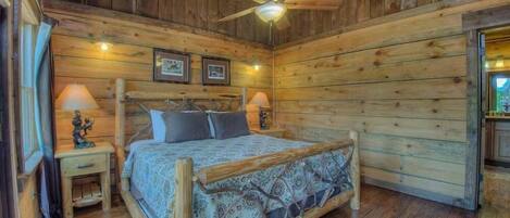 A wooden cabin bedroom with a bed, two nightstands, a ceiling fan, and framed pictures on the wall.