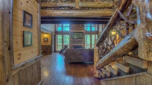 A log cabin interior with a stone fireplace, wooden floors, and a staircase with a wooden handrail. - Whitewater Wilderness- Riverside Retreat | Outdoor Living | Luxury Kitchen (Blue Ridge)