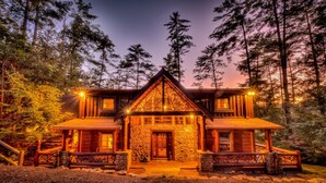 A log cabin with a stone facade, multiple windows, and a prominent front porch. - Whitewater Wilderness- Riverside Retreat | Outdoor Living | Luxury Kitchen (Blue Ridge)