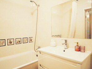 A bathroom with a bathtub, a sink with a mirror, and framed pictures on the wall.