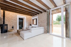 A modern living room with a stone wall, wooden beams, a white sofa, a fireplace, and a glass door leading outside.