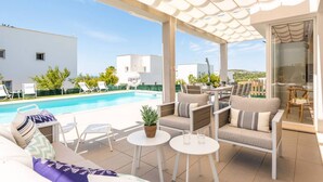 Ein überdachter Außenbereich mit Pool, Liegestühlen und einem Tisch mit Pflanze.