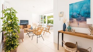 Ein modernes Wohnzimmer mit großem Fenster, einem Fernseher, Korbstühlen, einem Holztisch und einem Gemälde an der Wand.