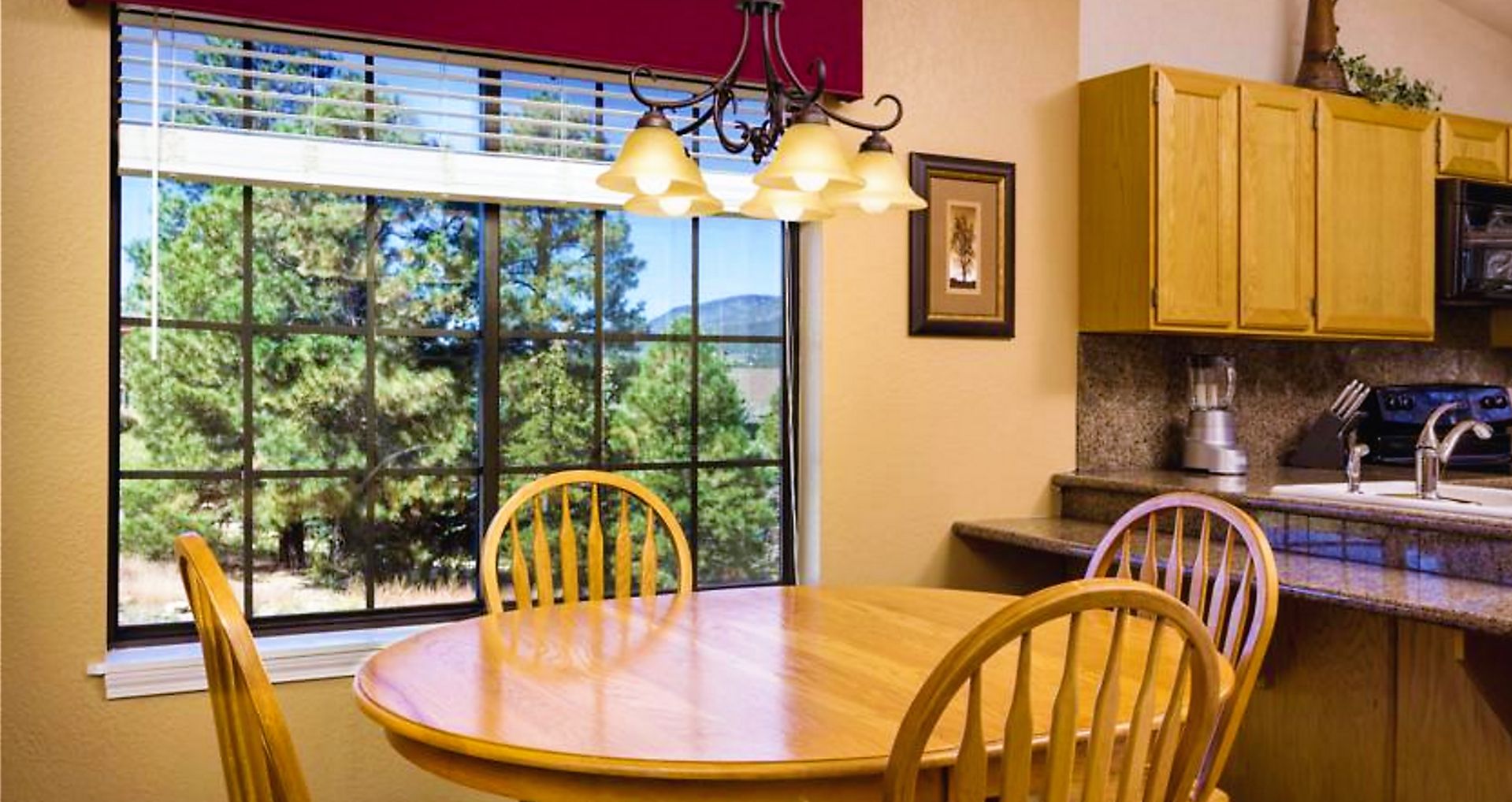 A dining area with a wooden table and chairs, a window with blinds, and a kitchen with wooden cabinets.