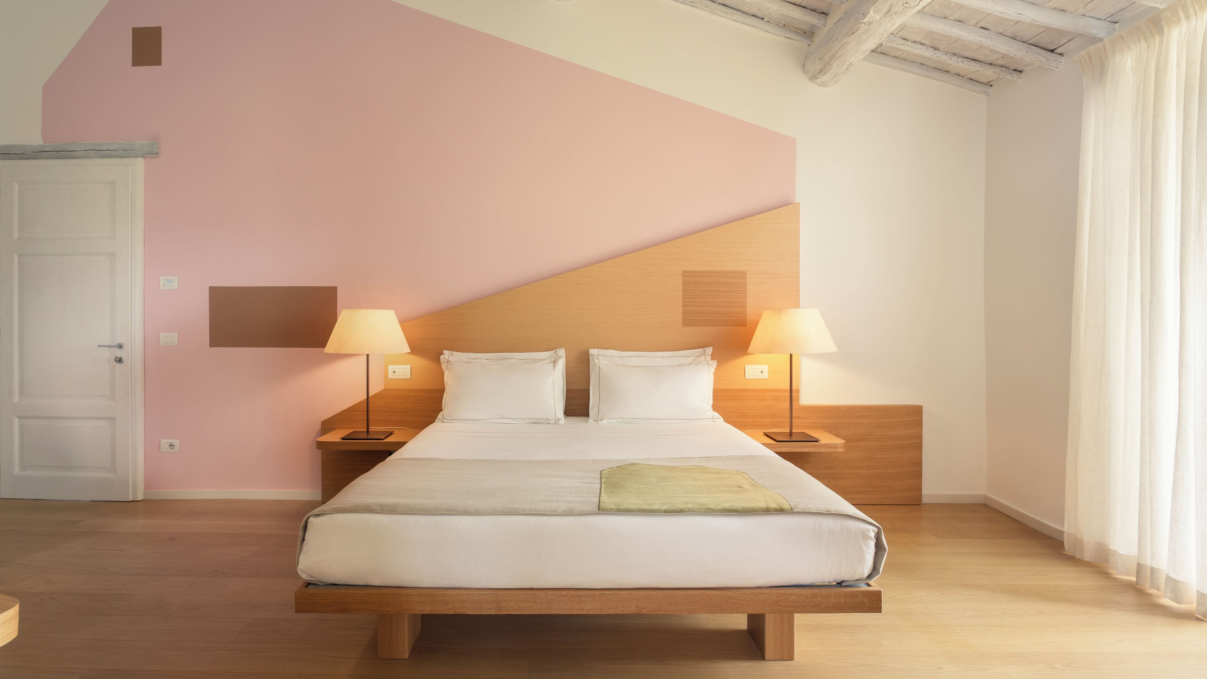 A bedroom with a wooden bed, two bedside tables with lamps, a white door, and a pink wall.