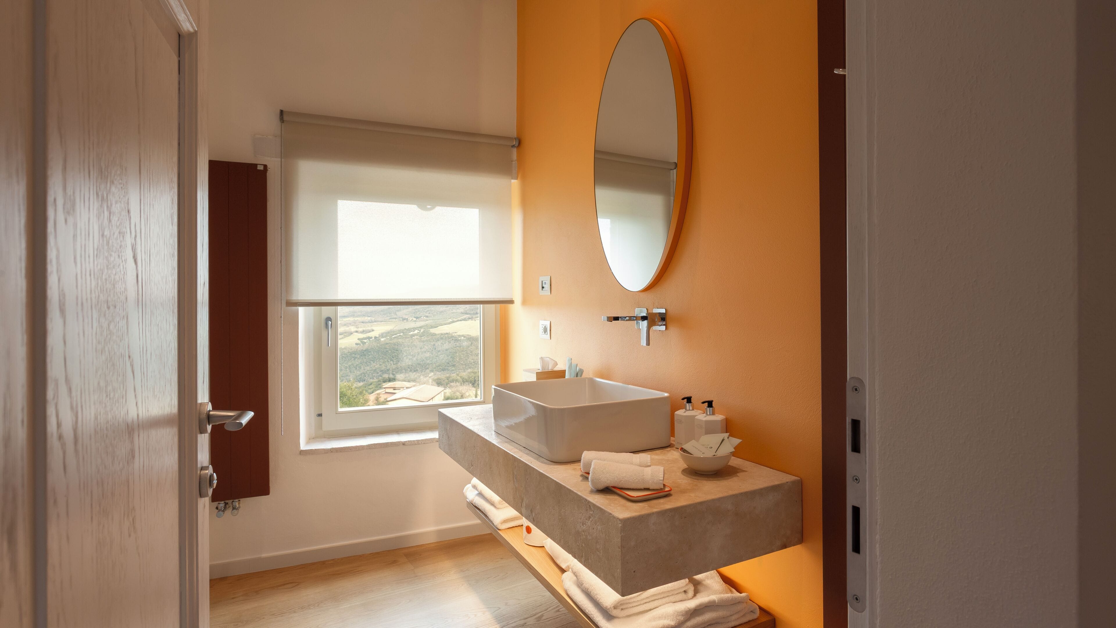 A bathroom with a large window, a bathtub, a vanity with a mirror, and a view of the outdoors.