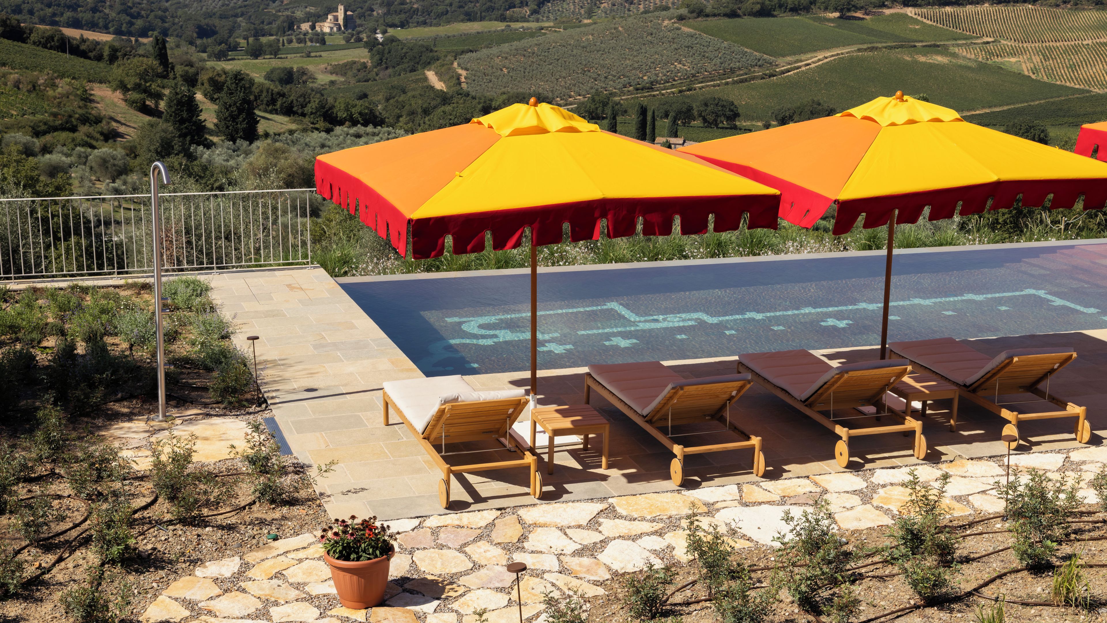 A poolside area with lounge chairs, umbrellas, and a view of vineyards.