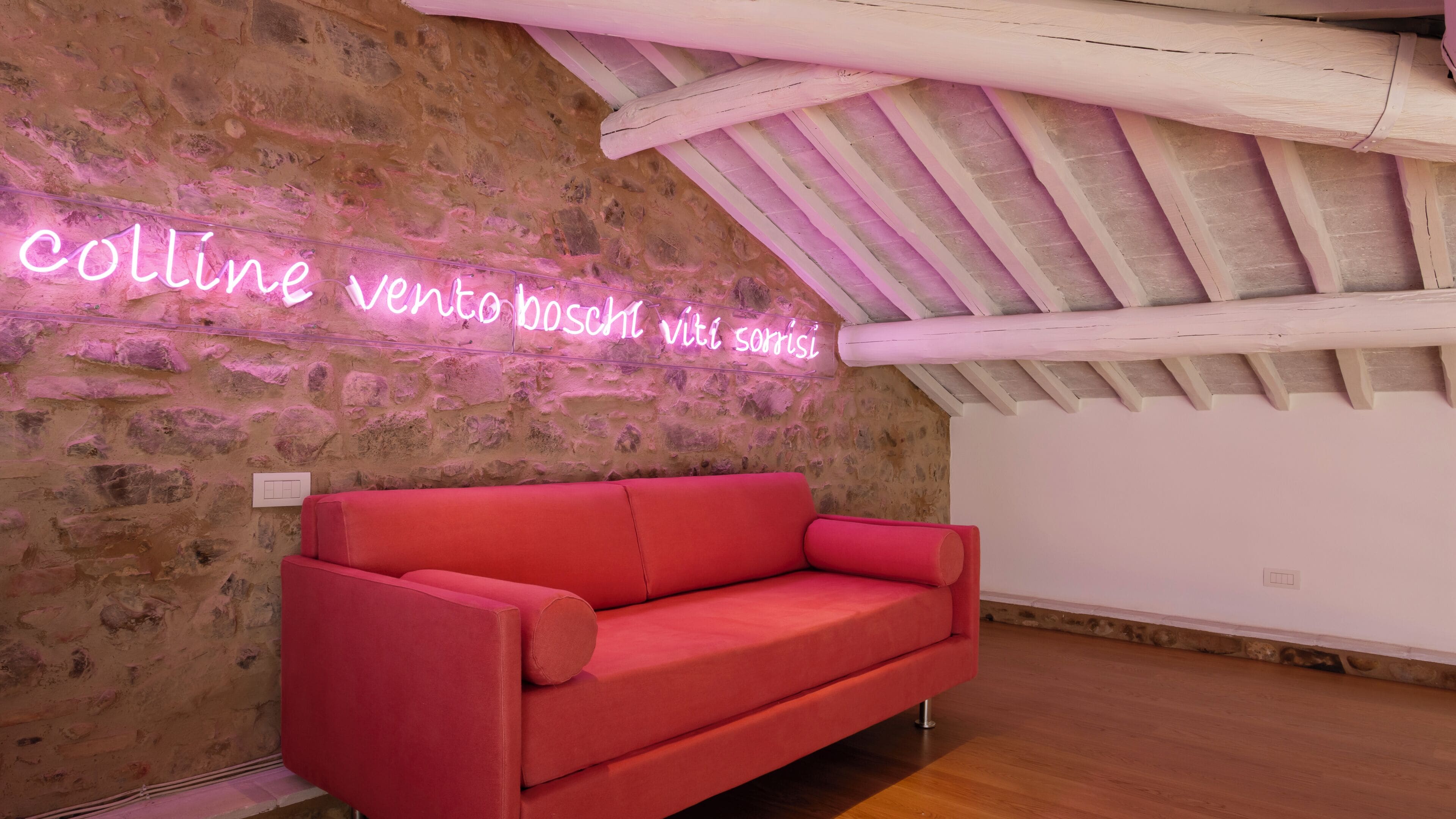 A room with a red sofa, a stone wall, and a neon sign.