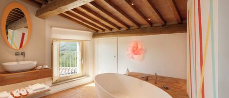 Un baño con una bañera independiente, un espejo grande y una ventana con vistas a una colina.