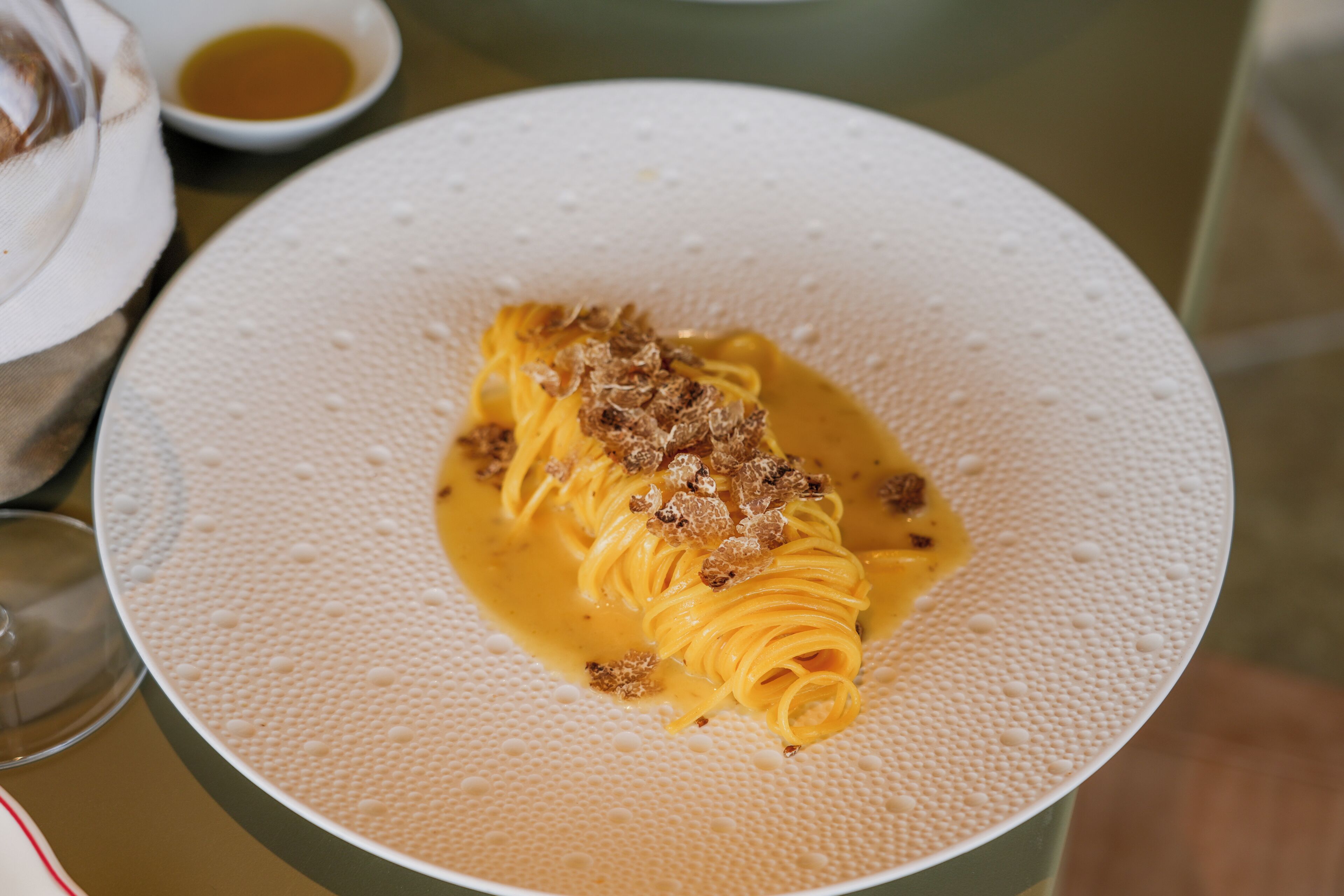 Une assiette de pâtes nappées d’une sauce crémeuse et saupoudrées de fromage râpé, le tout présenté dans une assiette blanche à texture.
