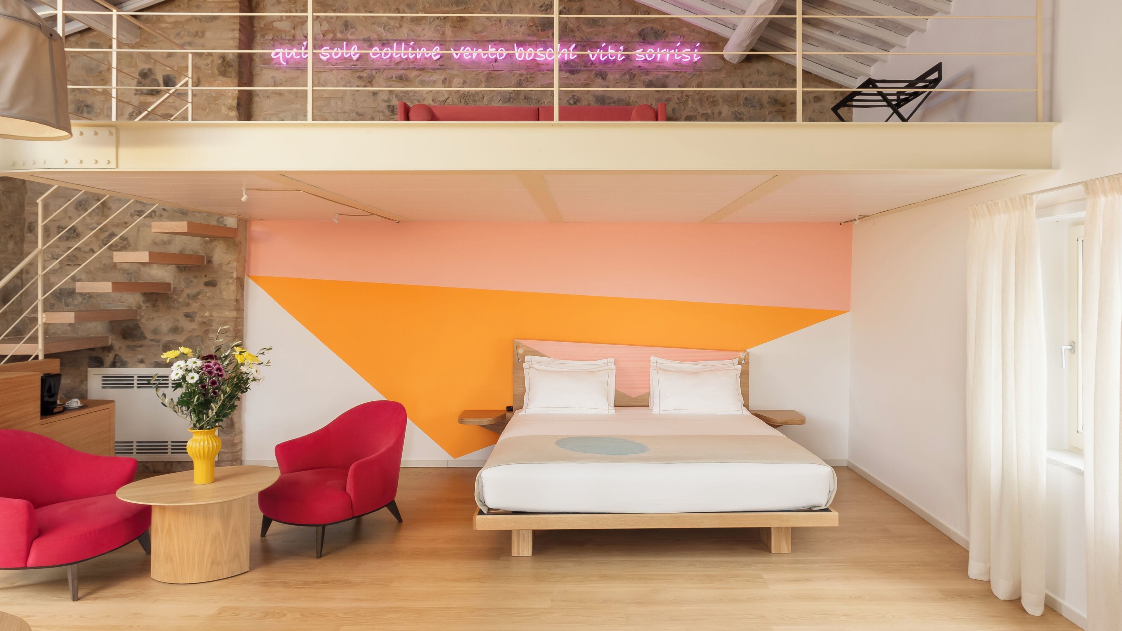 Habitación de hotel moderna con una cama, una silla roja, una mesita con un florero y una escalera.