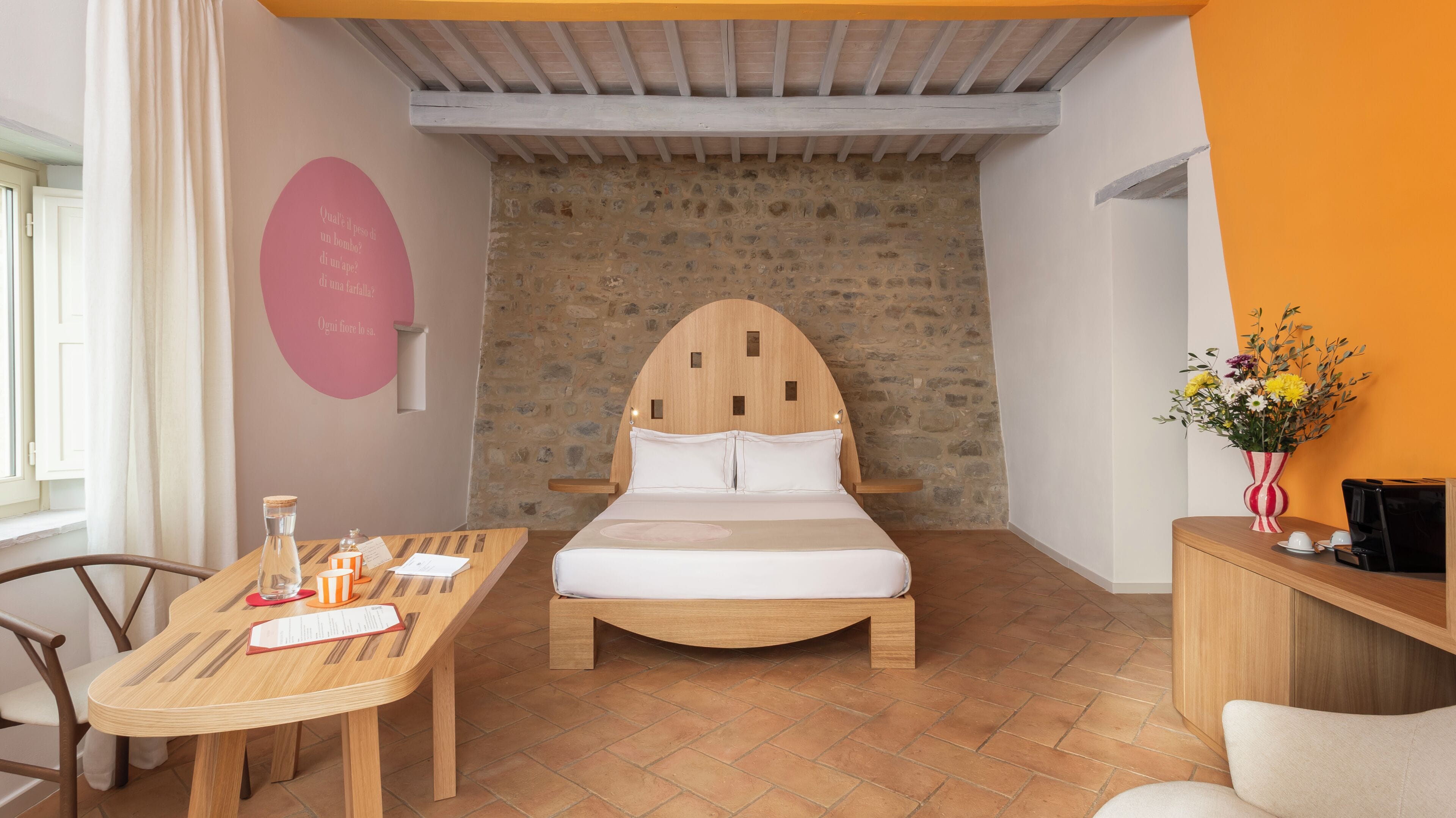 Un dormitorio con pared de piedra, cama de madera, escritorio de madera y una silla.
