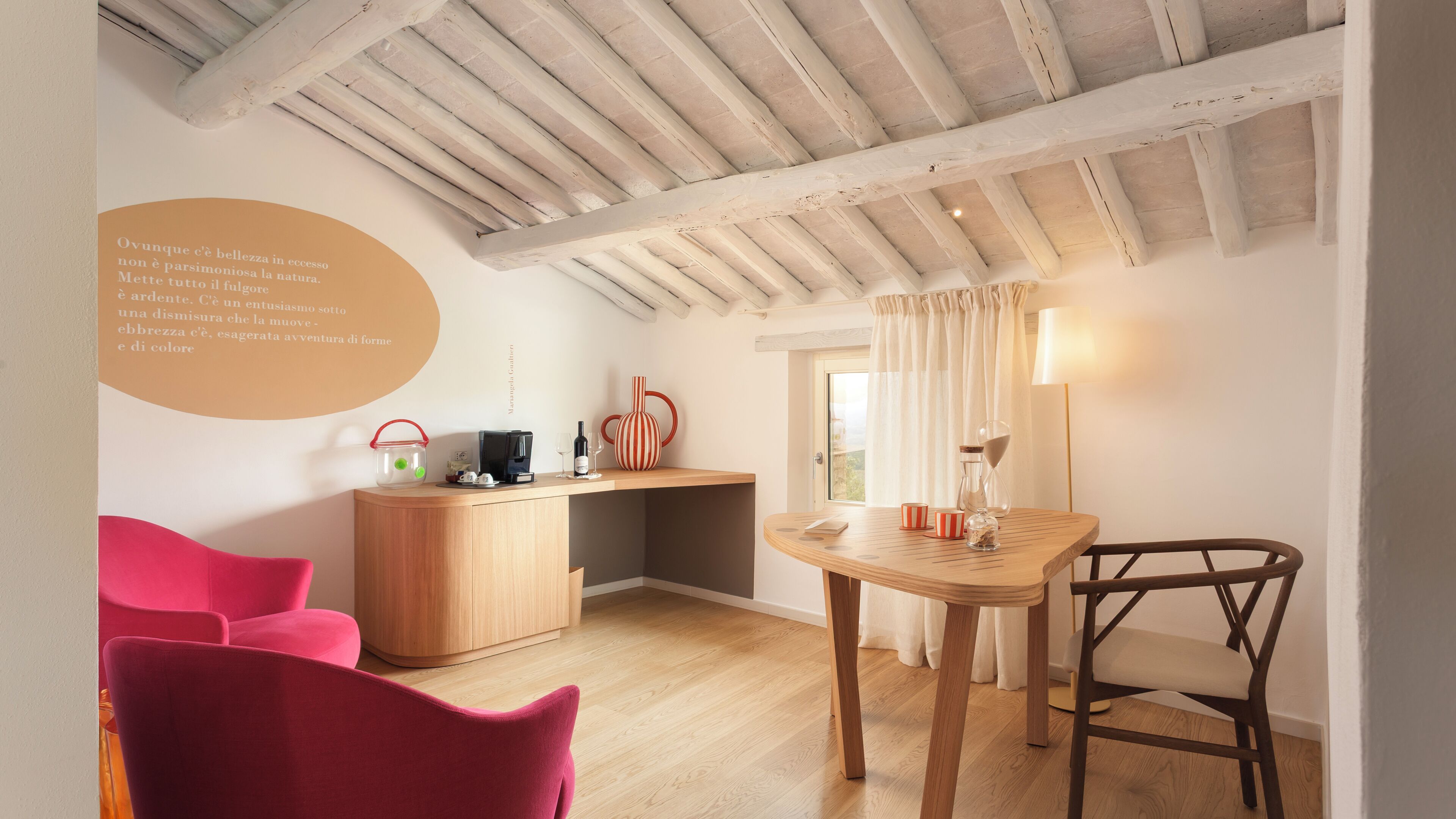 Una habitación con techo de madera, un escritorio con cafetera, una silla, una mesa y un sofá rosa.